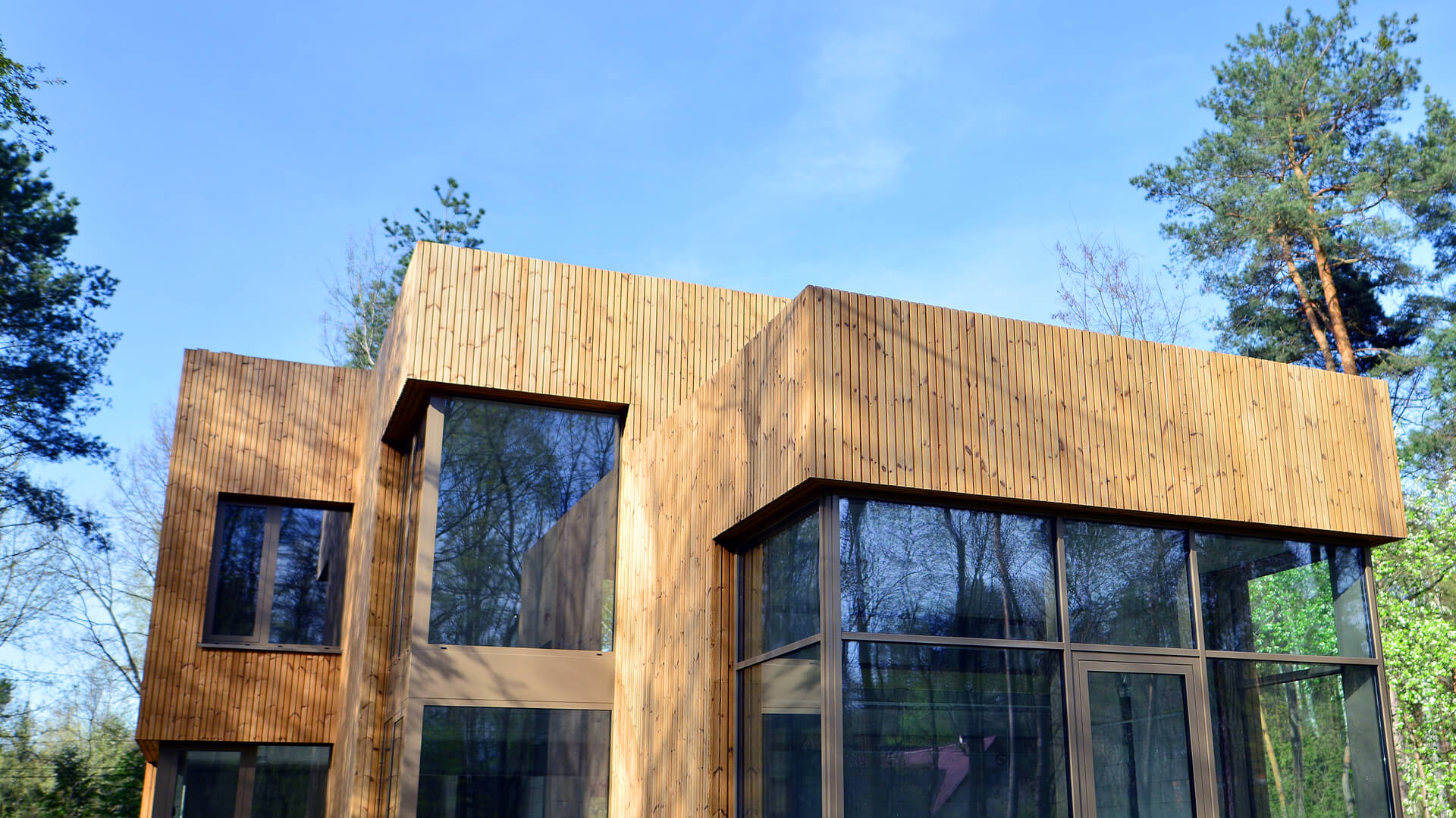 Modern house exterior with vertical timber cladding and large glass windows surrounded by trees.